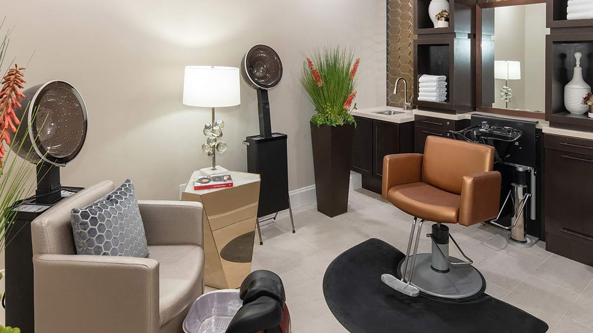 A cozy hair salon interior with seating, a lamp, and hairstyling equipment.