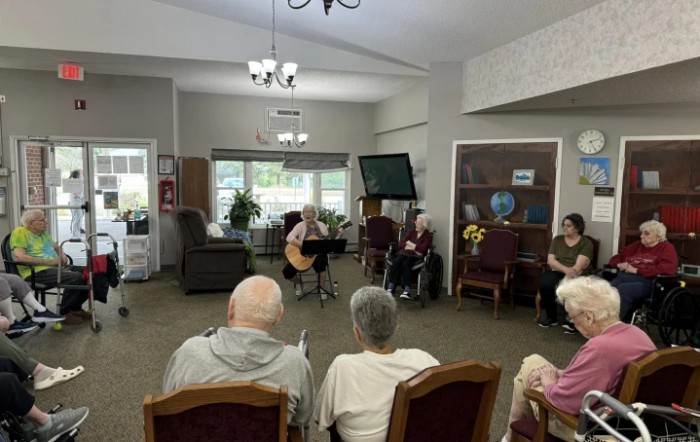 A musician performs for an audience of seniors in a community room.