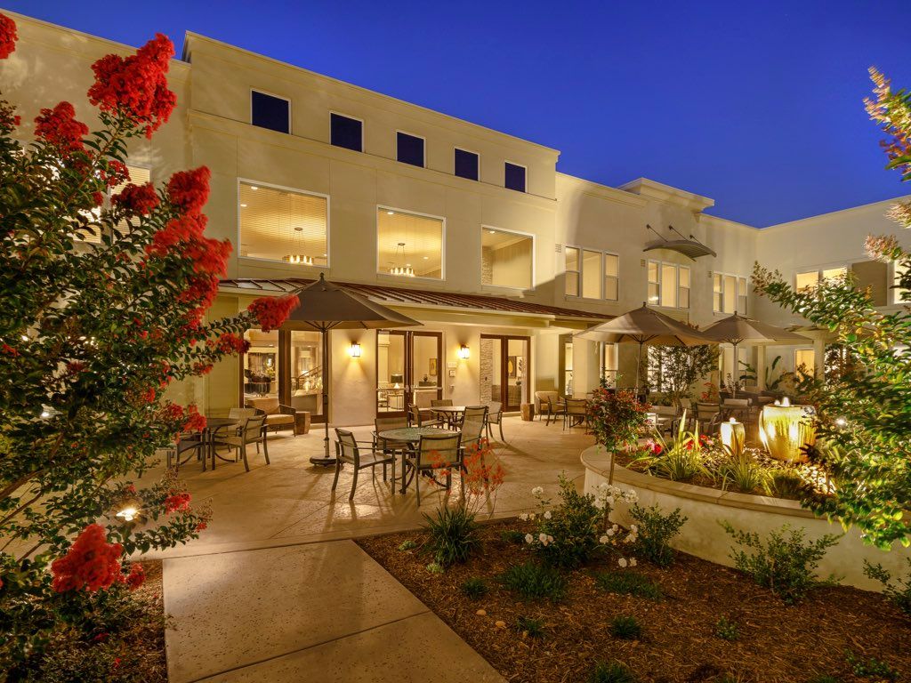 A beautifully lit luxury house with a spacious outdoor patio and garden at night.