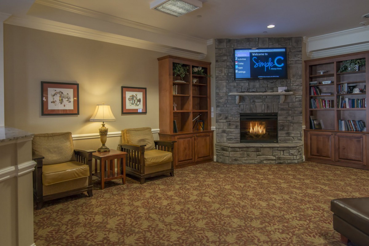 Cozy living room with a fireplace and television, featuring armchairs, a bookshelf, and framed pictures.