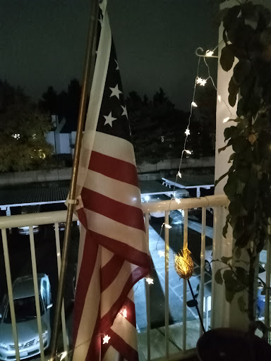 A United States flag gently waving on a balcony, illuminated by soft lights in the night.