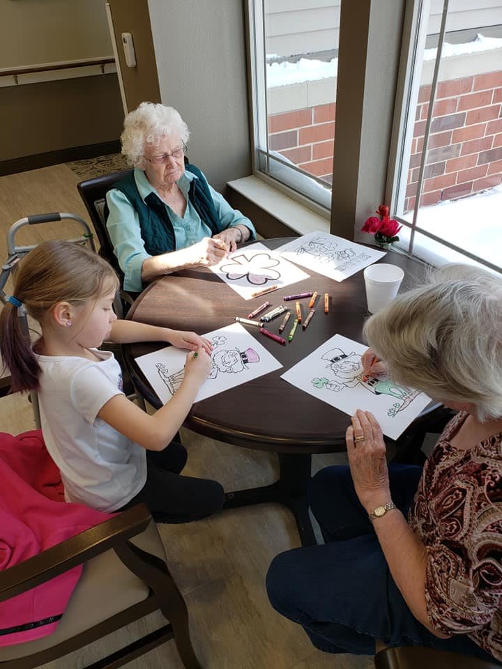 A young girl and two elderly women are engaging in a coloring activity together indoors.