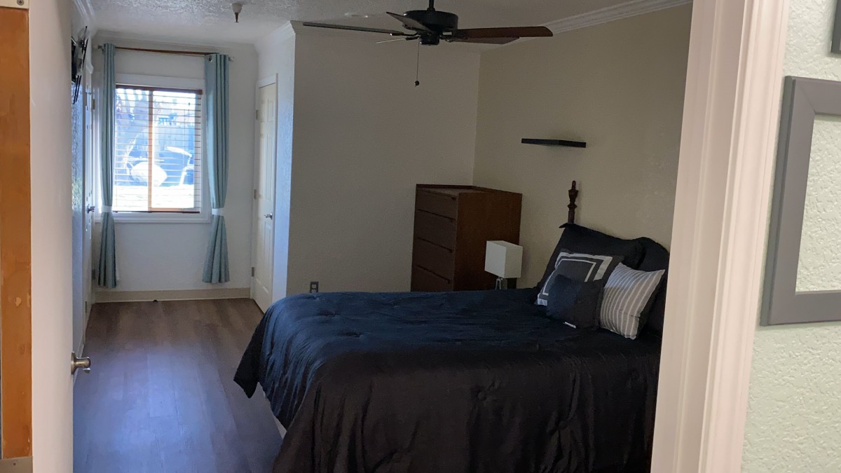 A modern bedroom with a neatly made bed, wooden furniture, and a ceiling fan.