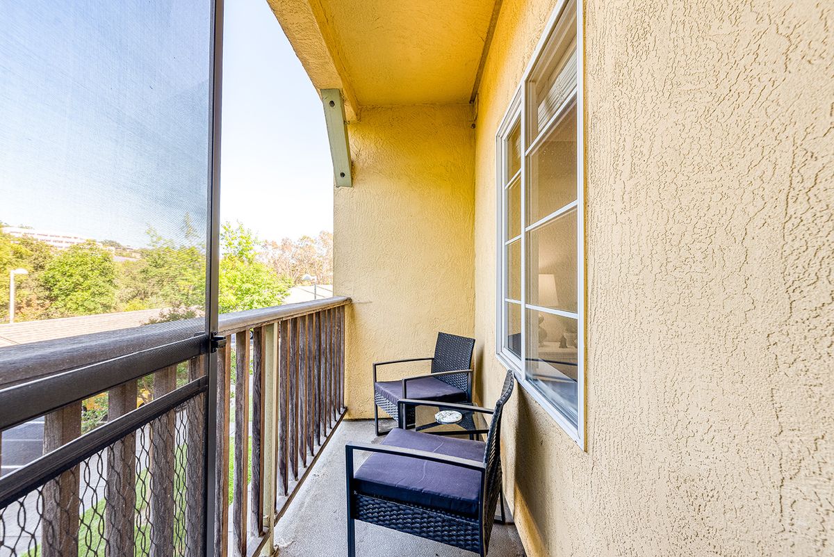 A sunny balcony with two chairs, overlooking a view through a railing.