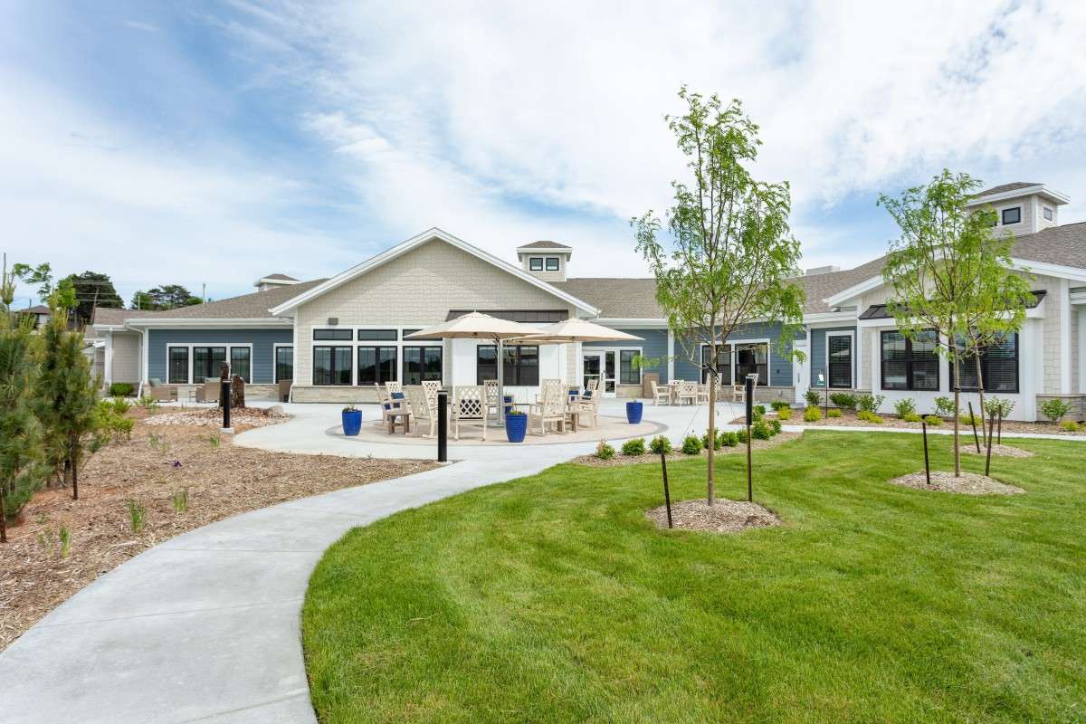 A modern building with a landscaped outdoor area featuring a lawn, trees, and a pathway.