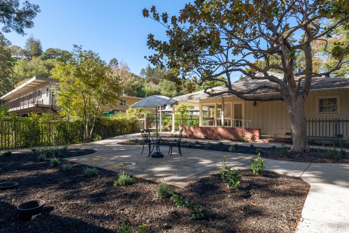 A tranquil patio area with outdoor seating surrounded by a lush garden and trees.
