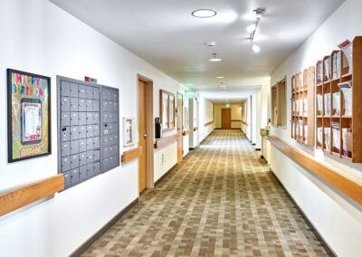 A well-lit, carpeted hallway with doors and mailboxes along the walls.