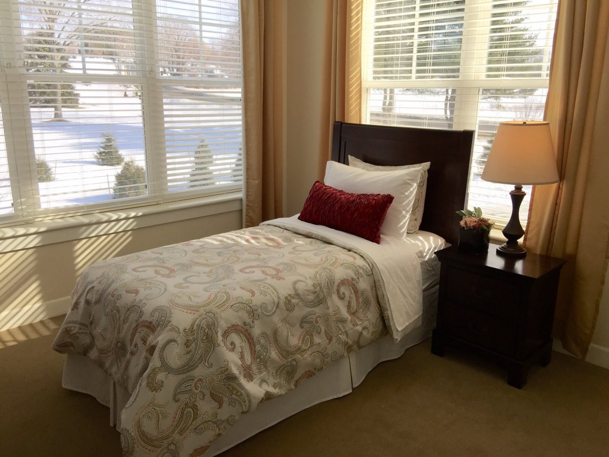 A cozy bedroom with a single bed next to a large window, featuring elegant decor and warm lighting.