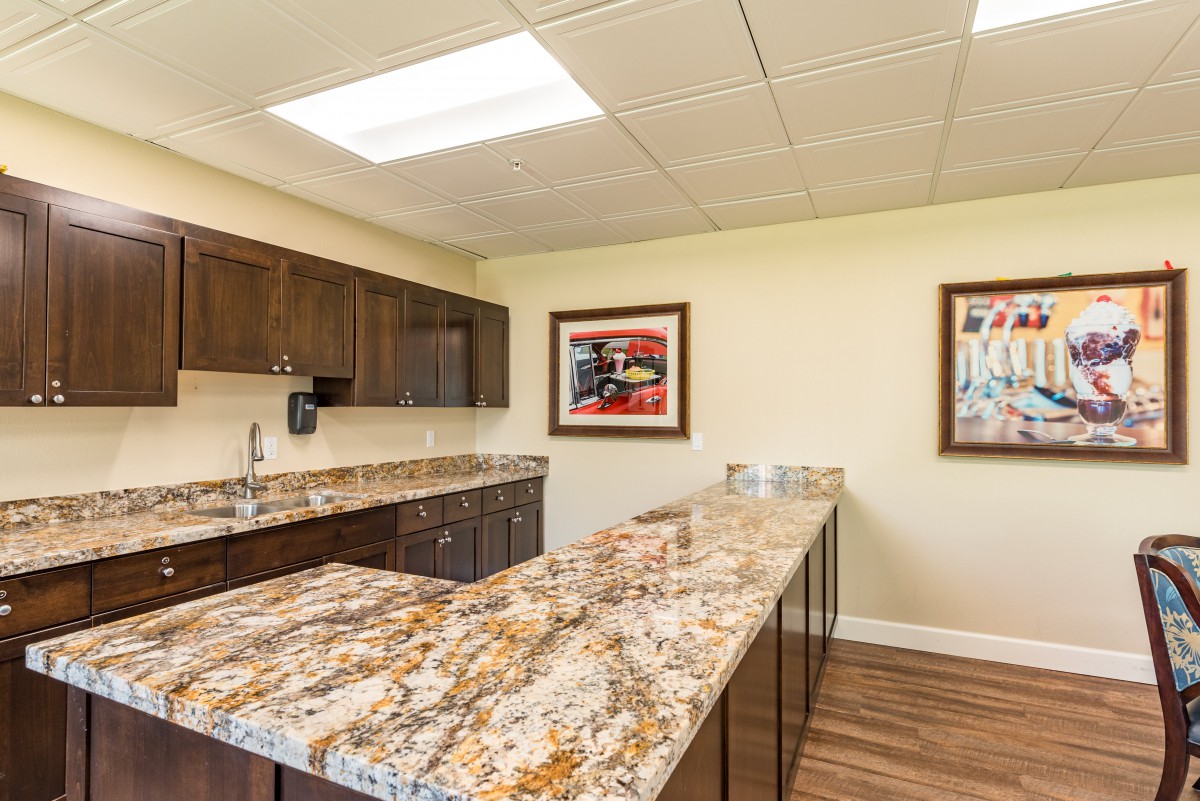 A modern office kitchen with granite countertops and artwork on the walls.