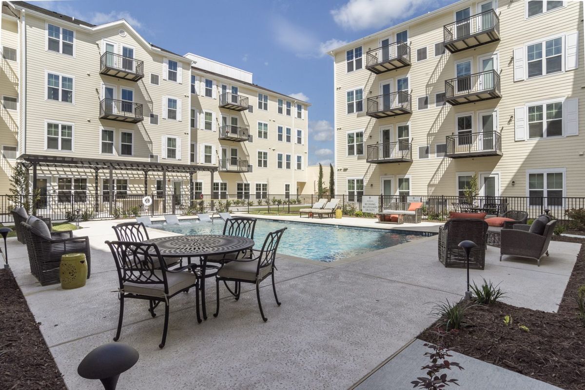 An outdoor view of an apartment complex featuring a swimming pool and patio furniture.