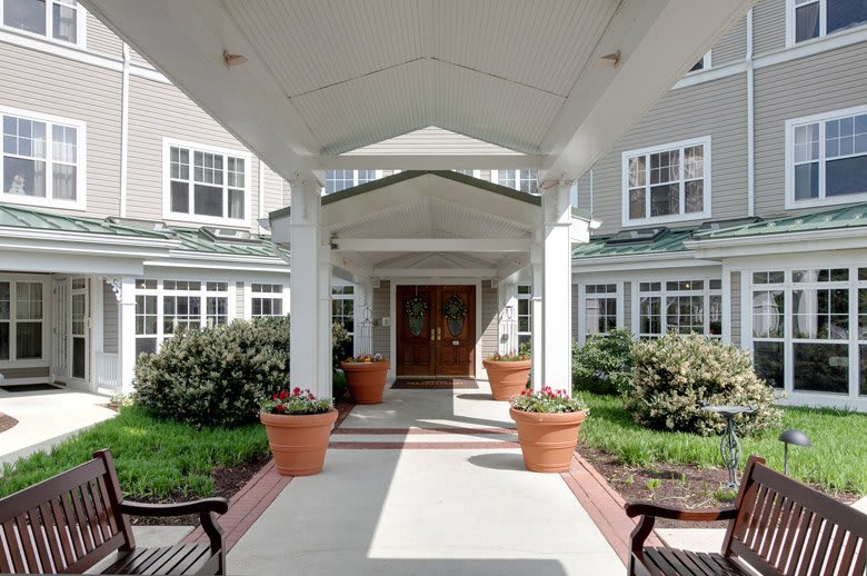 A covered entrance to a building with large potted plants on either side and well-maintained shrubbery.
