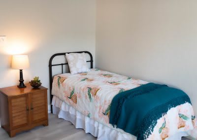 A simple bedroom with a single bed, nightstand, and lamp.