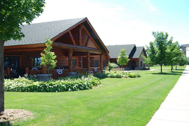 A row of log cabins surrounded by well-maintained lawns and greenery.