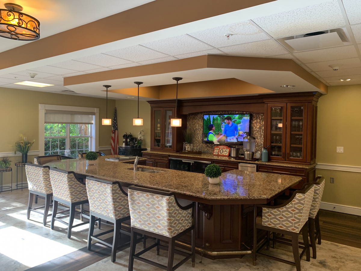 A cozy indoor bar with a long counter, wicker chairs, and a television on the wall.