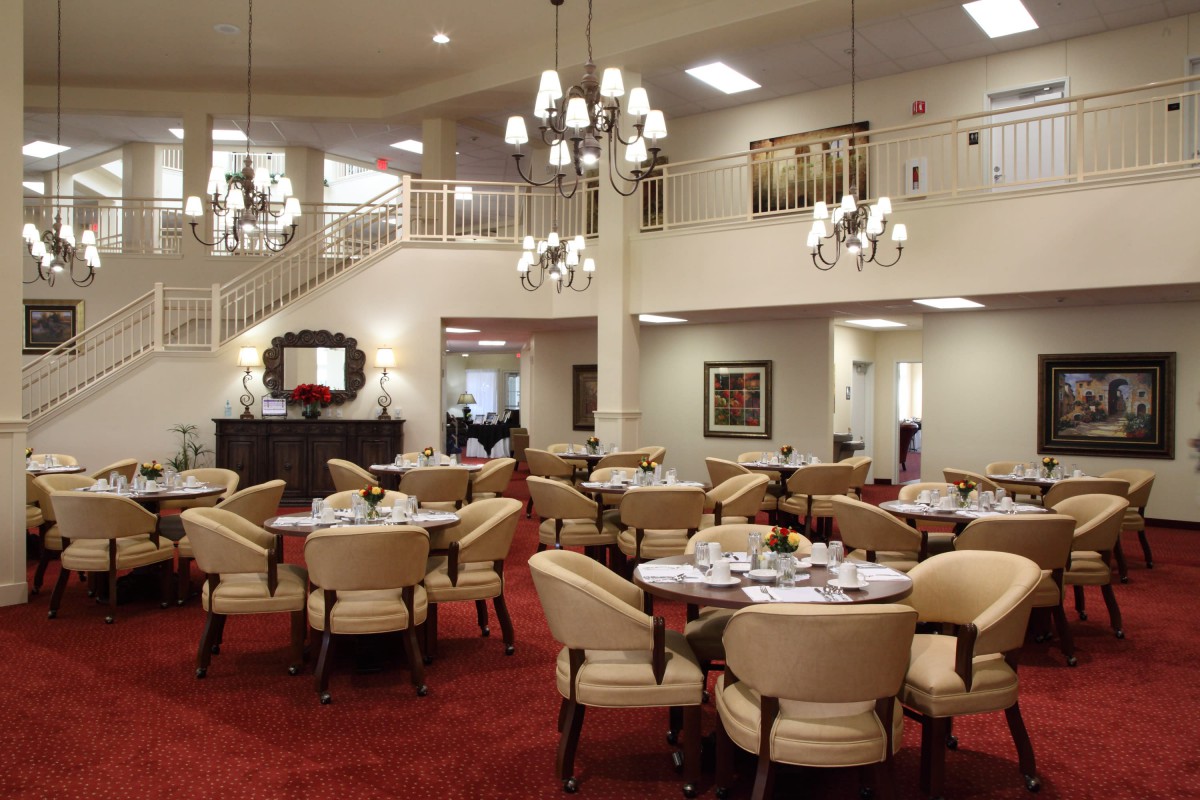 An elegant dining room with multiple tables and chairs, adorned with chandeliers and a red carpet.