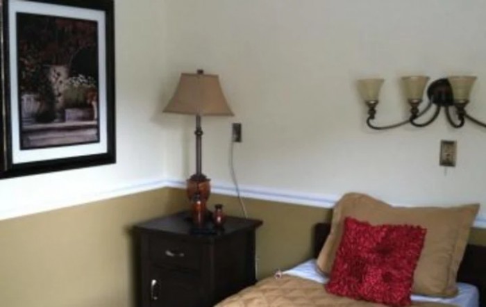 A cozy bedroom corner with a lamp on a nightstand beside a bed.