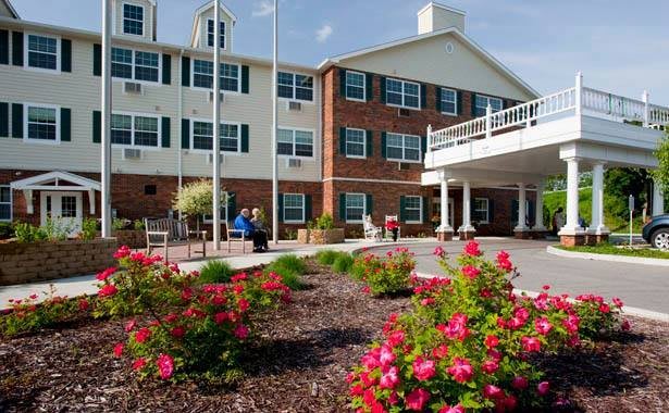 A landscaped garden with blooming flowers in front of a multi-story brick and white building.
