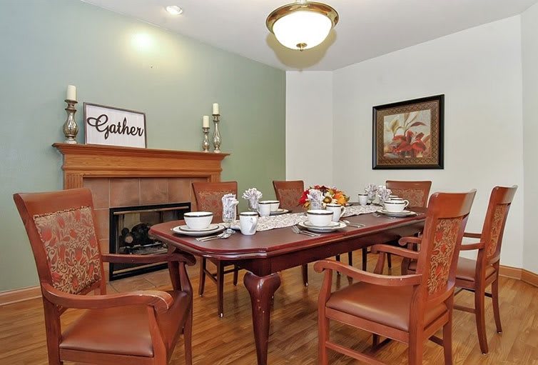 A cozy dining room featuring a wooden dining table set with dishes, surrounded by chairs and accented by a fireplace and wall art.