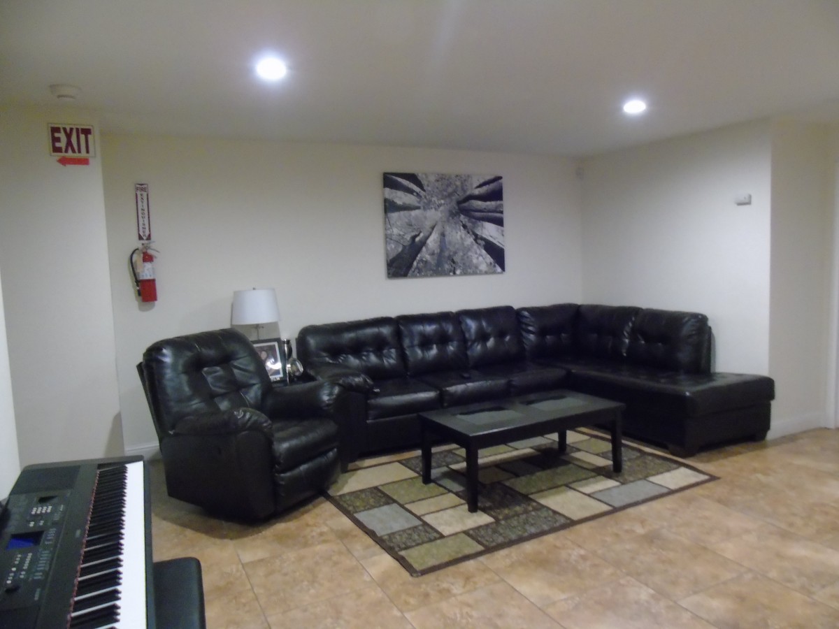 A cozy living room with a black leather sectional, coffee table, and guitar hanging on the wall.