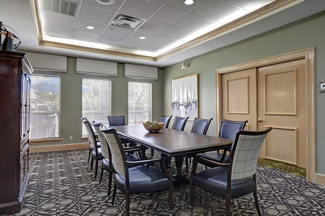 A modern conference room featuring a large table surrounded by chairs, with natural light streaming through multiple windows.