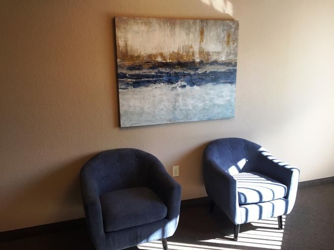 A cozy waiting area with two blue chairs and a contemporary painting on the wall.