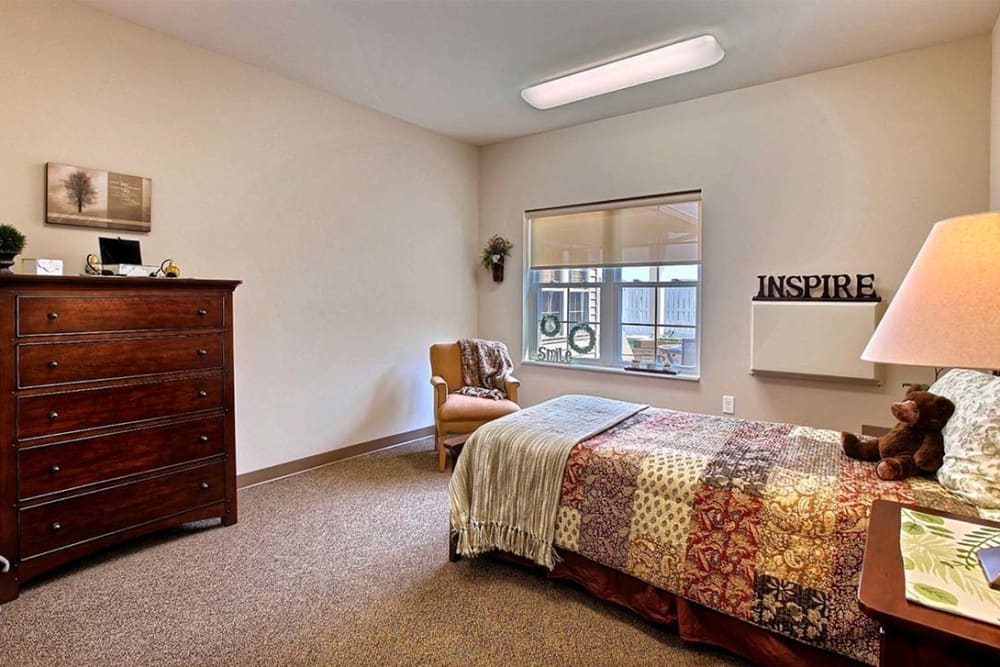 A cozy bedroom with a colorful bedspread, a dresser, and a window with natural light.