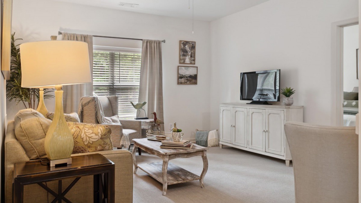A cozy living room with a sofa, coffee table, and TV, featuring soft lighting from a lamp by the window.