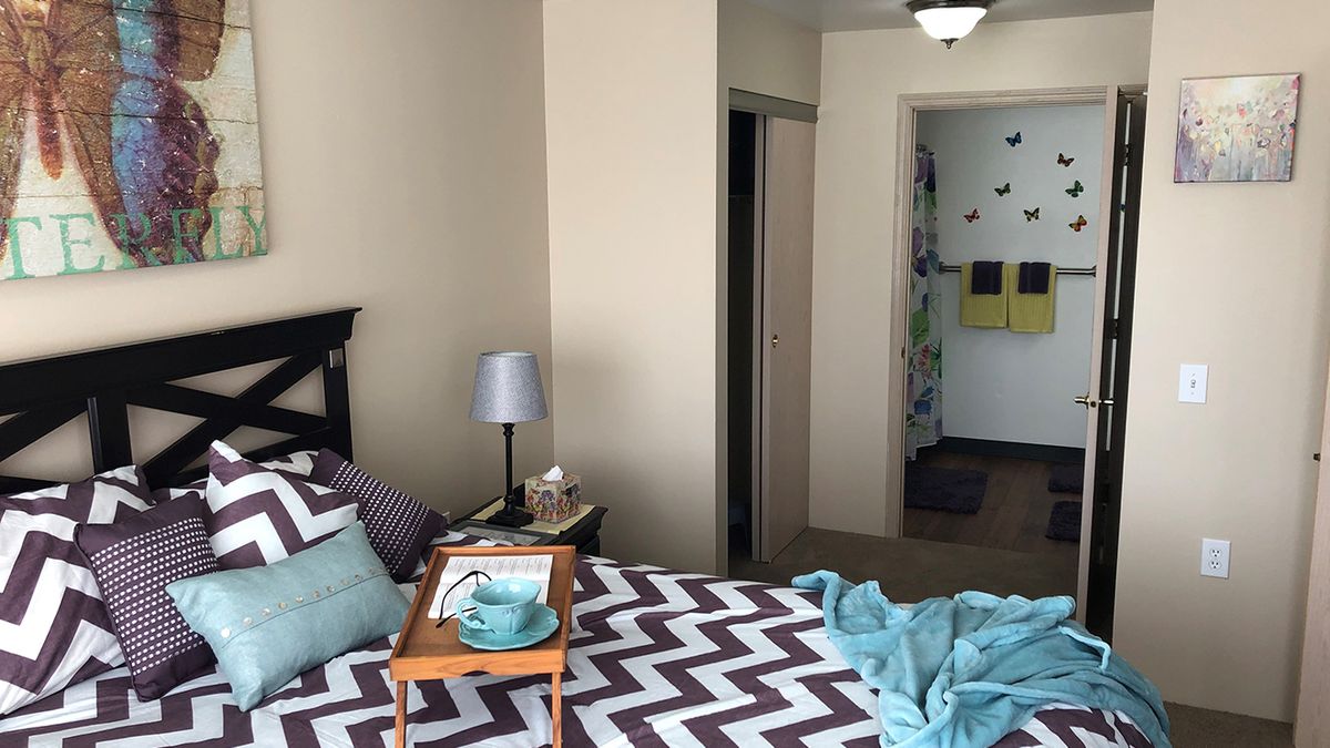A cozy bedroom with a zigzag patterned bedspread, pillows, and a bedside lamp.