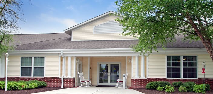 A building entrance with rocking chairs on the porch and columns supporting the roof.