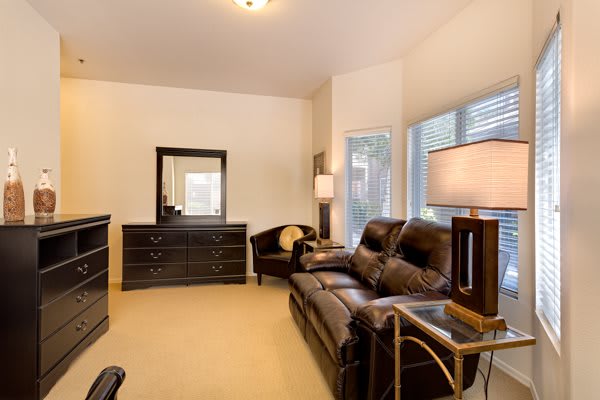 A cozy living room with a leather couch, multiple lamps, and a dresser with an overhead mirror.