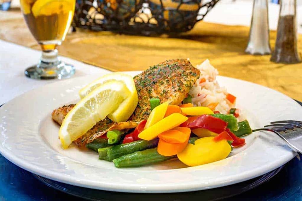 A colorful plate featuring grilled salmon, assorted steamed vegetables, and lemon wedges.