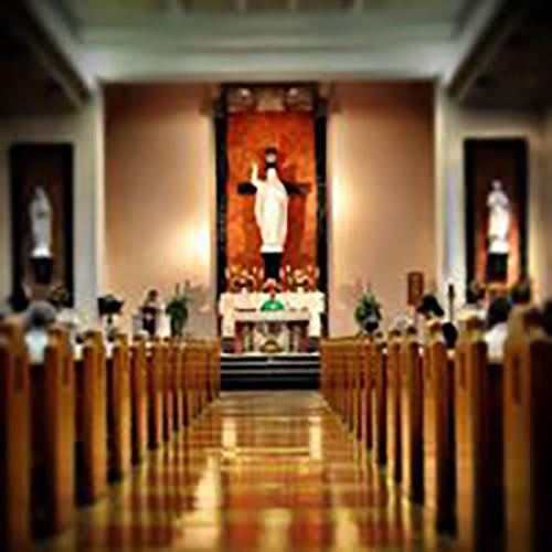 A view of the interior of a church, showcasing rows of pews leading to an altar with religious statues.