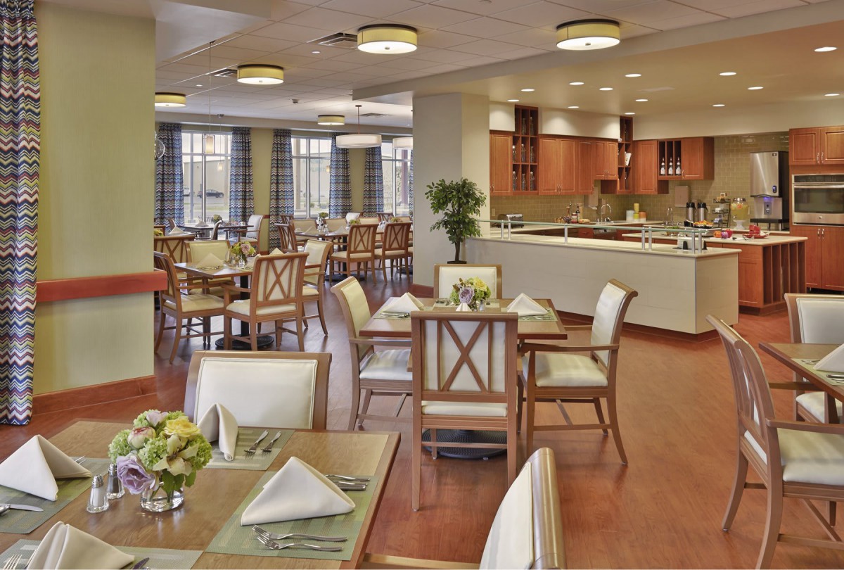 A modern restaurant dining area with neatly arranged tables and chairs, featuring a view of the open kitchen.