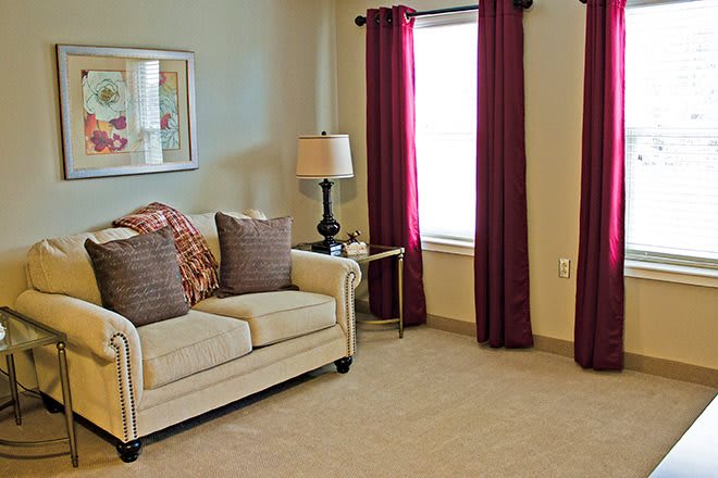 A cozy living room with a beige sofa, decorative pillows, a lamp, and burgundy curtains.