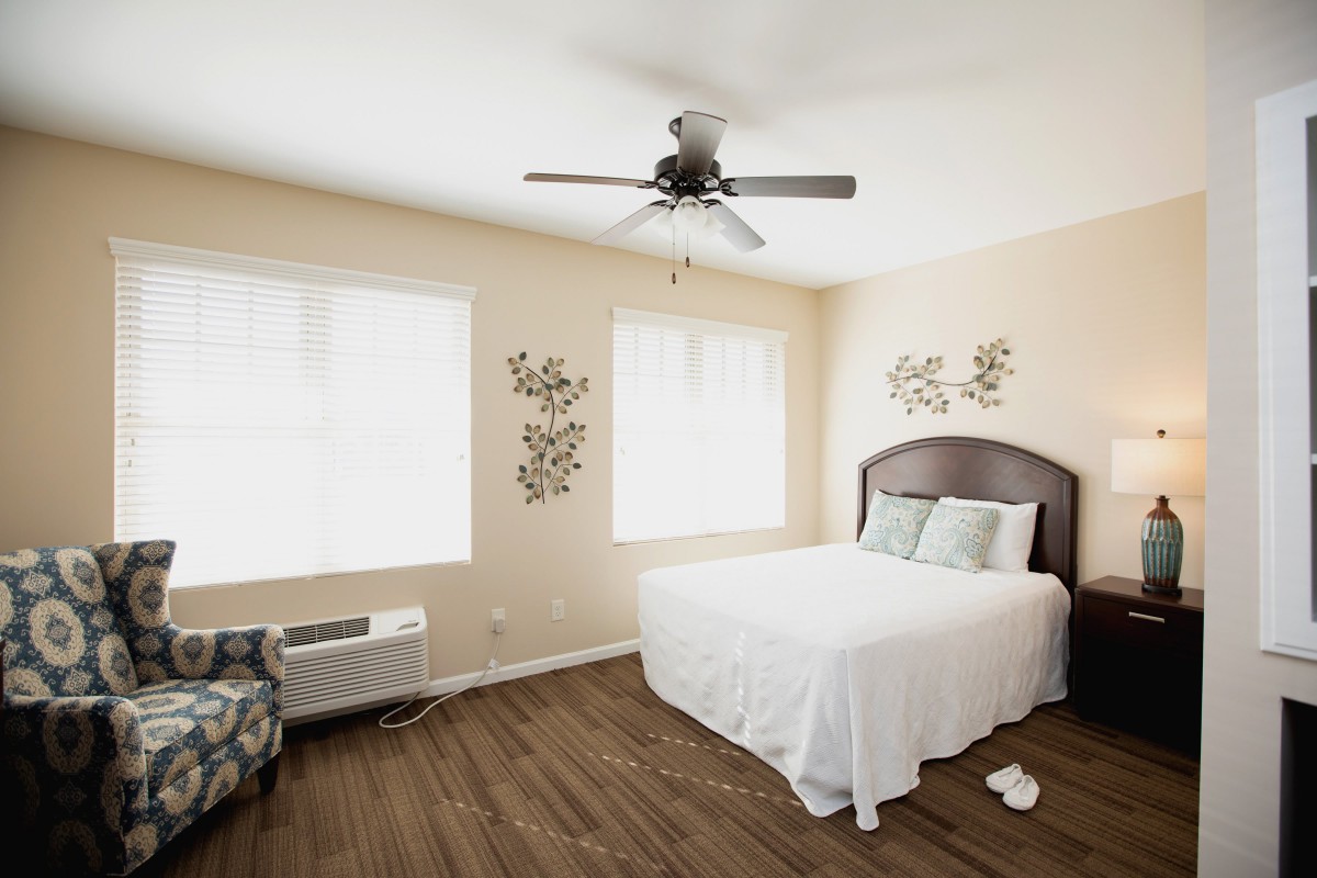 A bright and minimalist bedroom with a neatly made bed, ceiling fan, and decorative wall art.