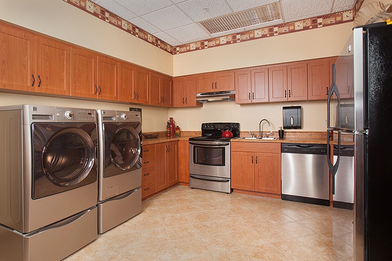 A modern kitchen featuring stainless steel appliances, including a washer and dryer, with wooden cabinets and a decorative border.