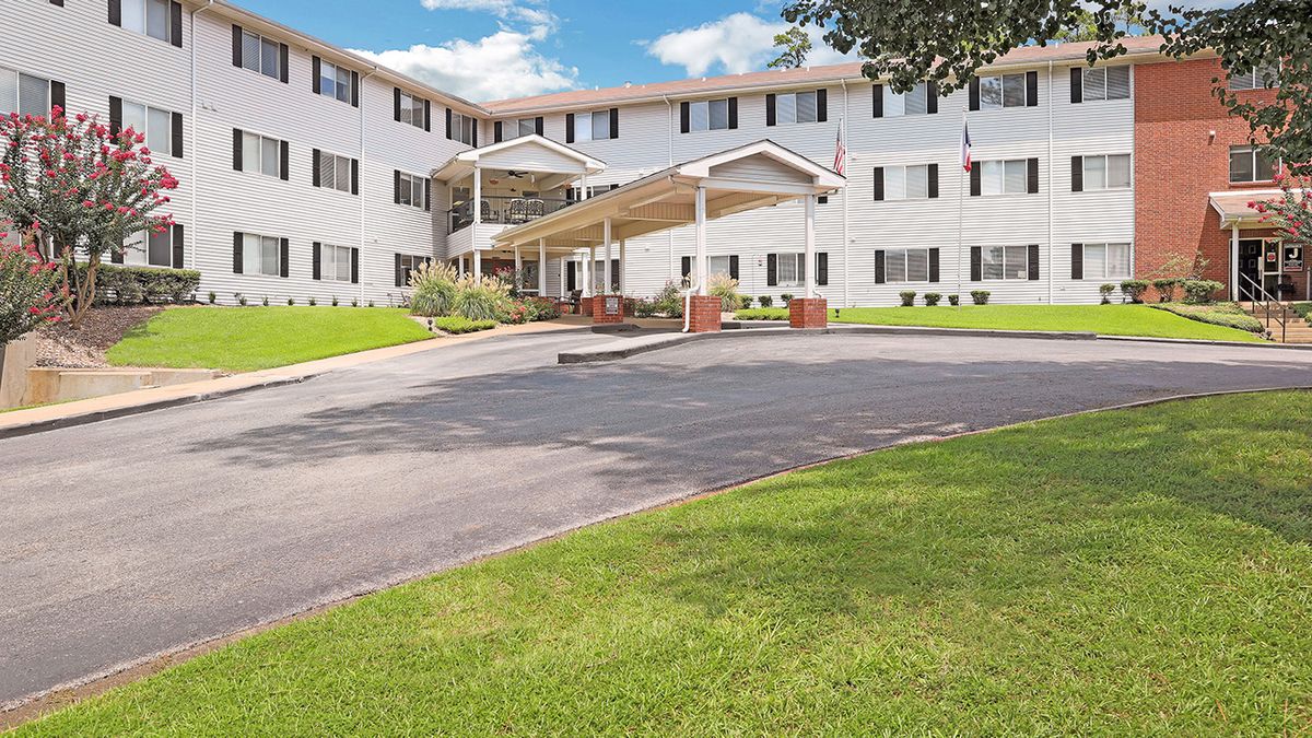 A sunny day view of a residential apartment building with a well-maintained lawn and driveway.
