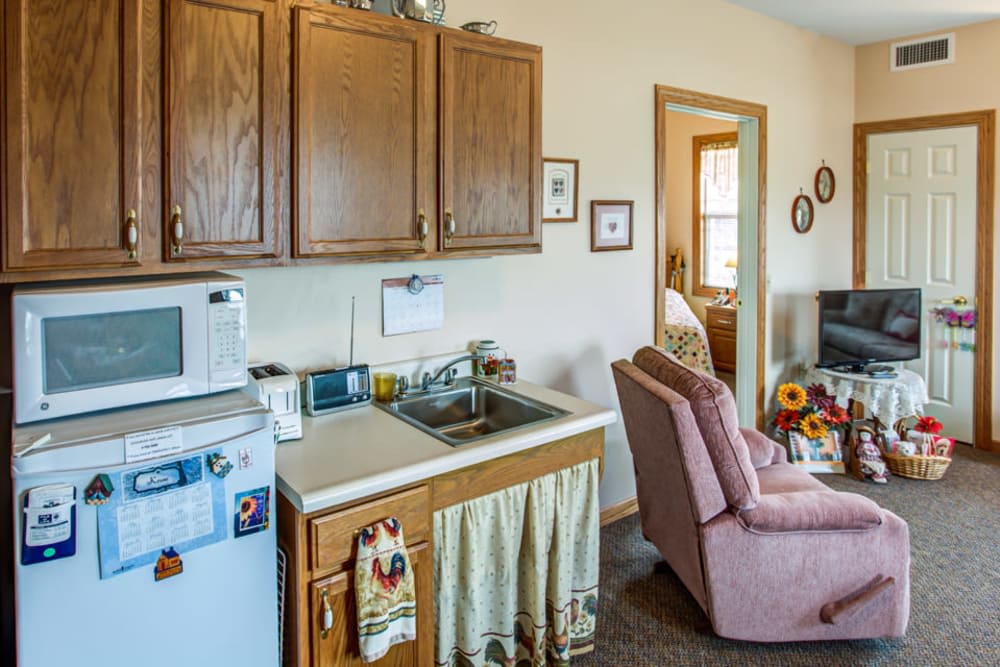 A cozy kitchen and living room area with wooden cabinets, a sink, microwave, and a comfortable chair.