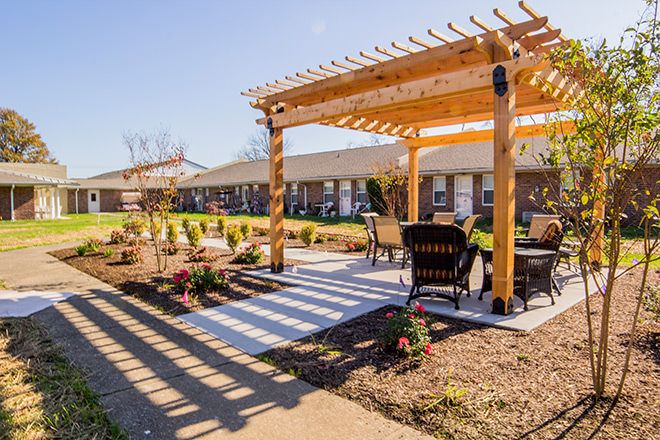 A cozy outdoor area featuring a wooden pergola with comfortable seating and a beautifully landscaped garden on a sunny day.