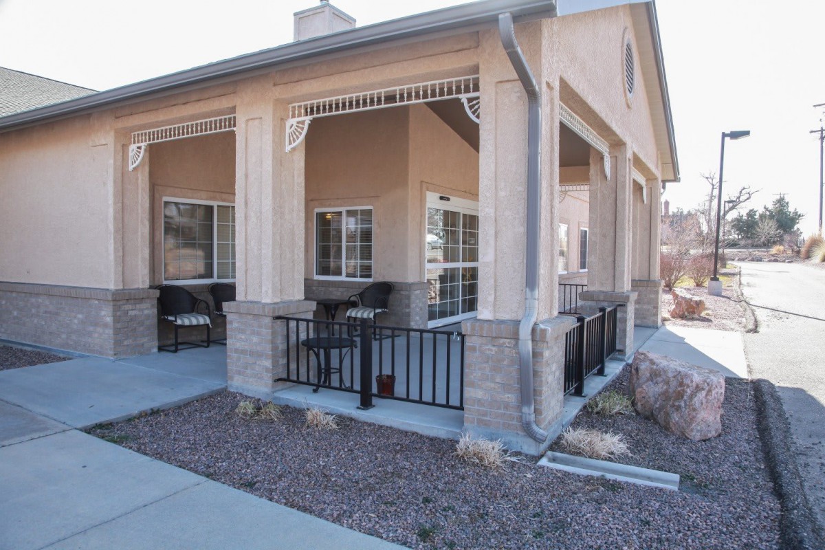 A residential building with a covered porch featuring outdoor seating and fenced area.