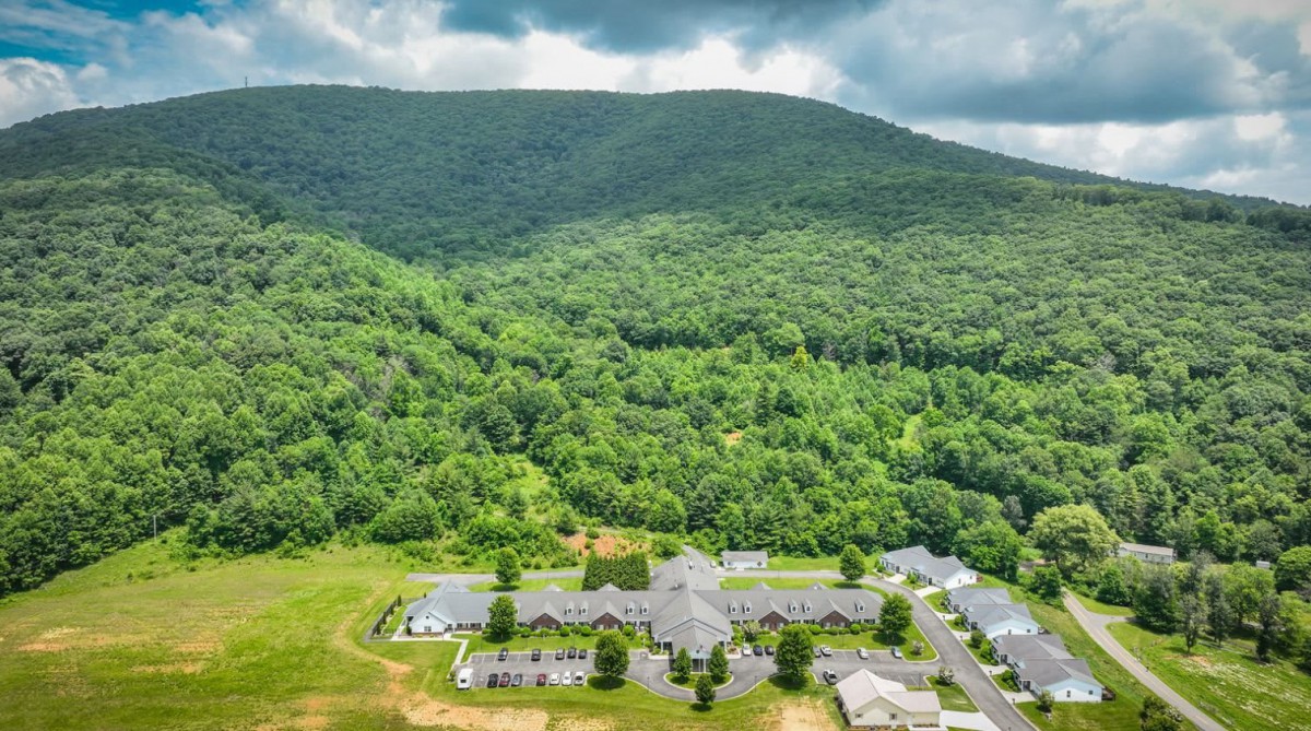 Aerial view of buildings nestled amidst lush green mountains and forested countryside.