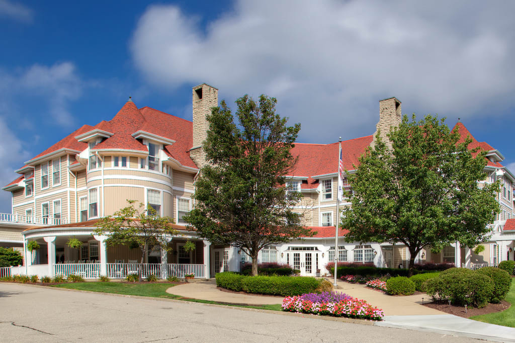 A large, elegant building with a red roof surrounded by trees and landscaping under a partly cloudy sky.