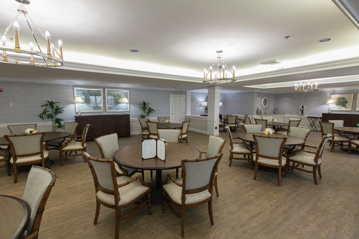 A well-lit dining room with several tables and chairs arranged on a wooden floor.