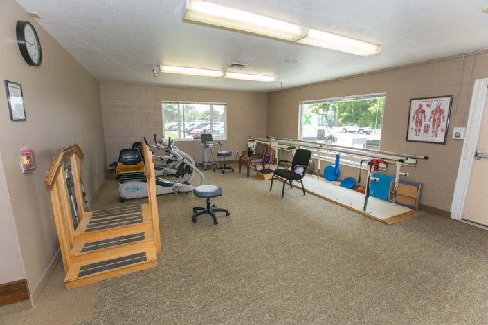 A rehabilitation room equipped with exercise machines, stairs, and parallel bars for physical therapy.