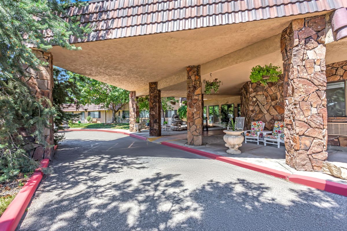 A covered entrance with stone columns and outdoor seating, surrounded by landscaping.