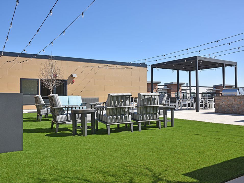 A rooftop patio with seating areas and artificial grass under a clear blue sky.
