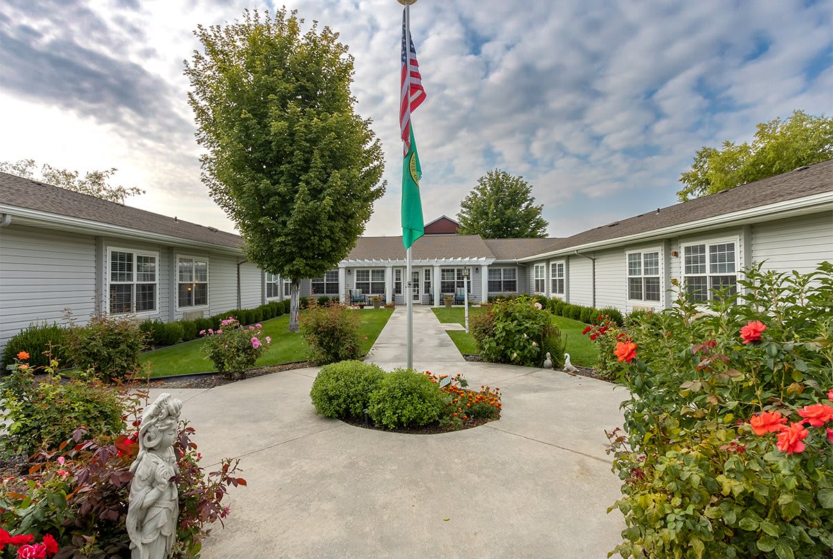 A well-maintained courtyard with a central pathway leading to a building, featuring an American flag and manicured gardens.