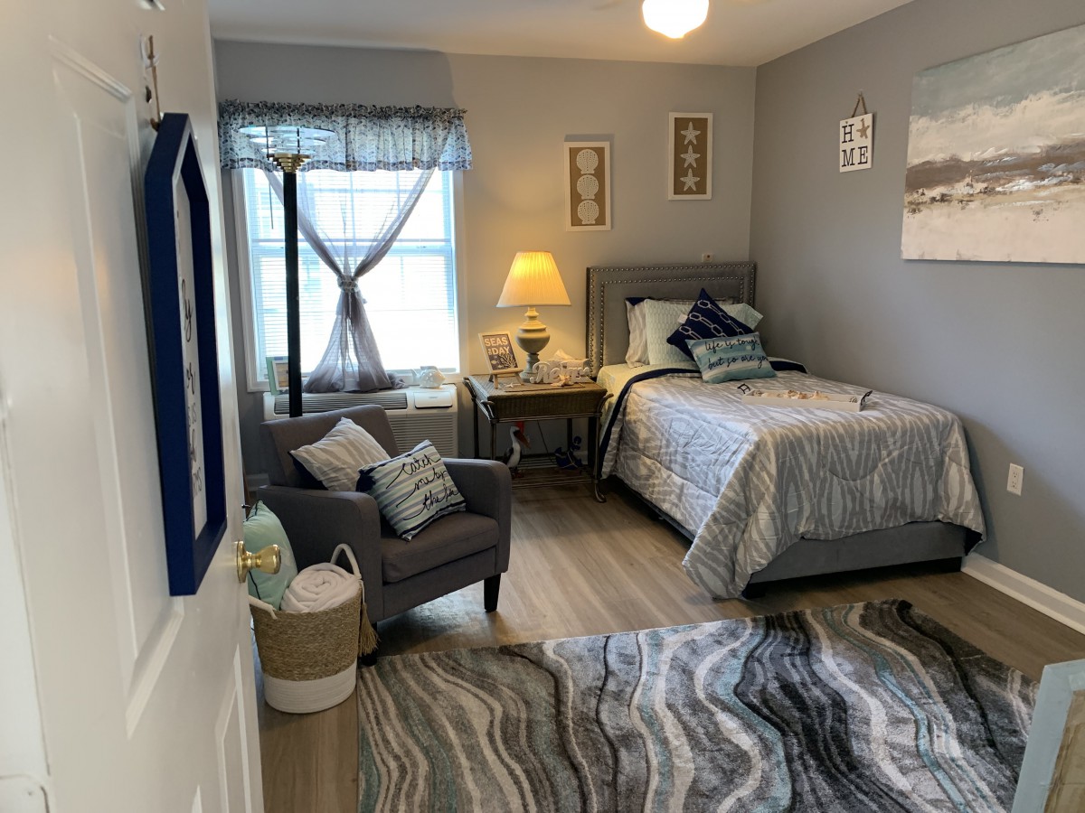 A cozy and well-decorated bedroom with grey walls, featuring a bed, chair, lamp, and window.