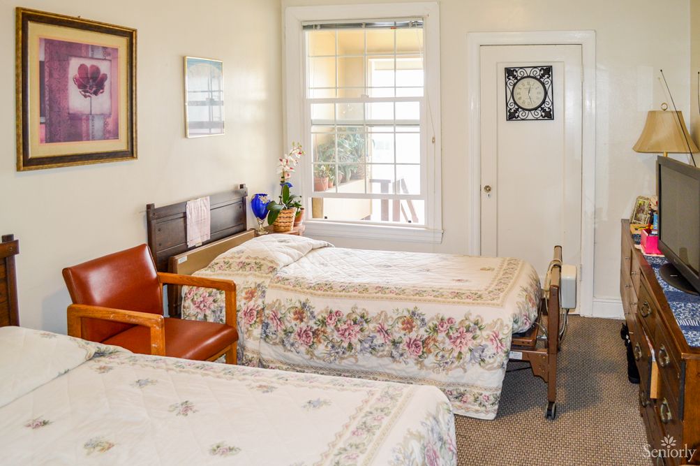 A cozy bedroom with two twin beds featuring floral bedding, a wooden bench, and a large window.