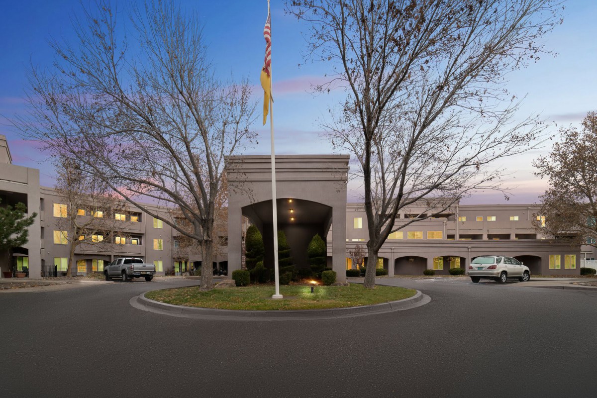 An elegant building entrance with a flagpole and surrounding trees at dusk.